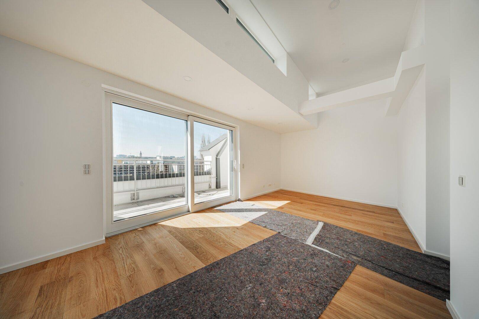 Helles, leeres Zimmer mit Holzboden und Schiebetür zum Balkon, ideal für Schlaf- oder Arbeitsbereich.