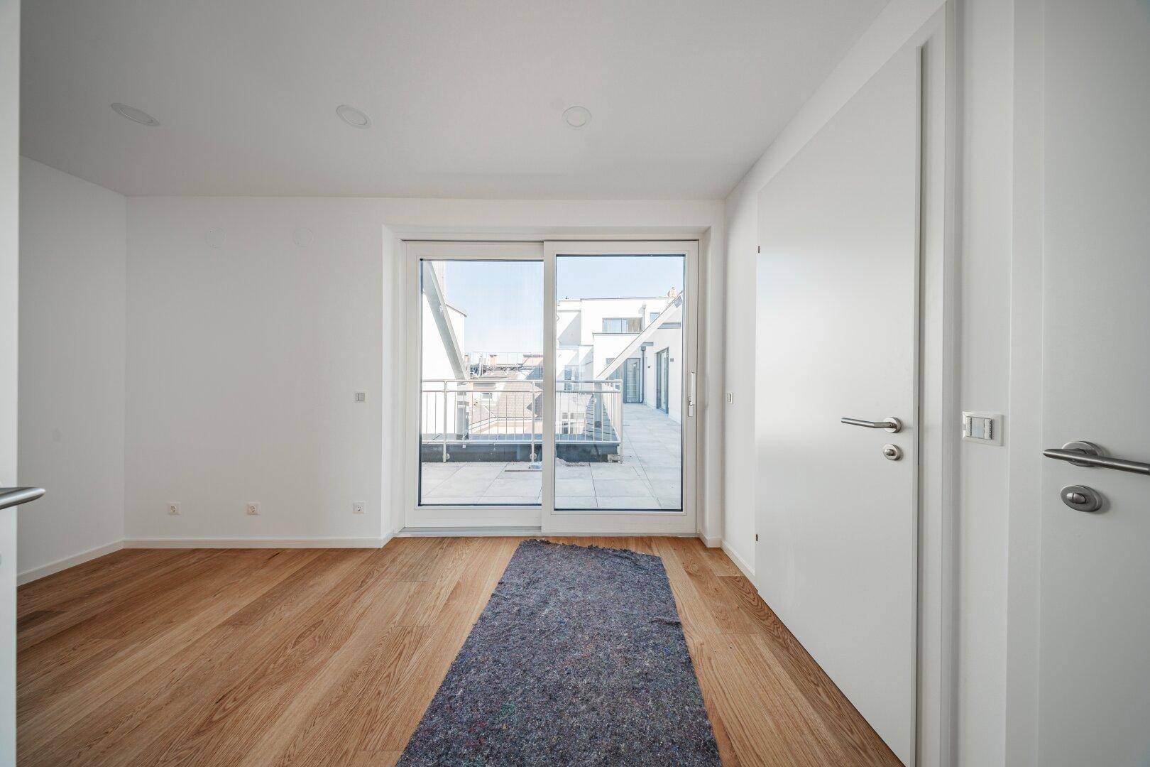 Sonniger, leerer Raum mit Holzboden und Zugang zu einem Balkon, ideal als Schlafzimmer.