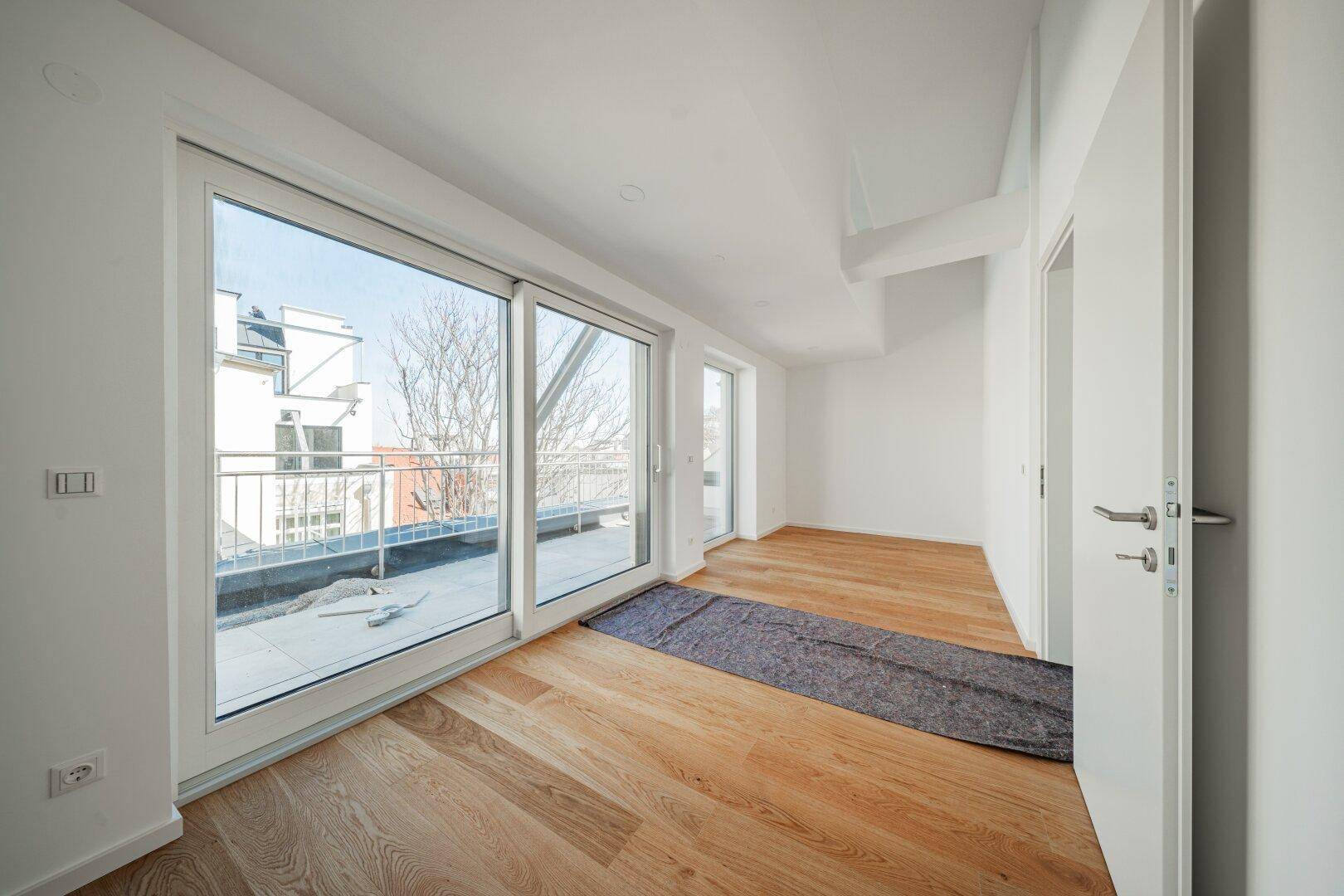 Geräumiges, helles Zimmer mit Holzboden und großen Fenstern, die viel Licht spenden.