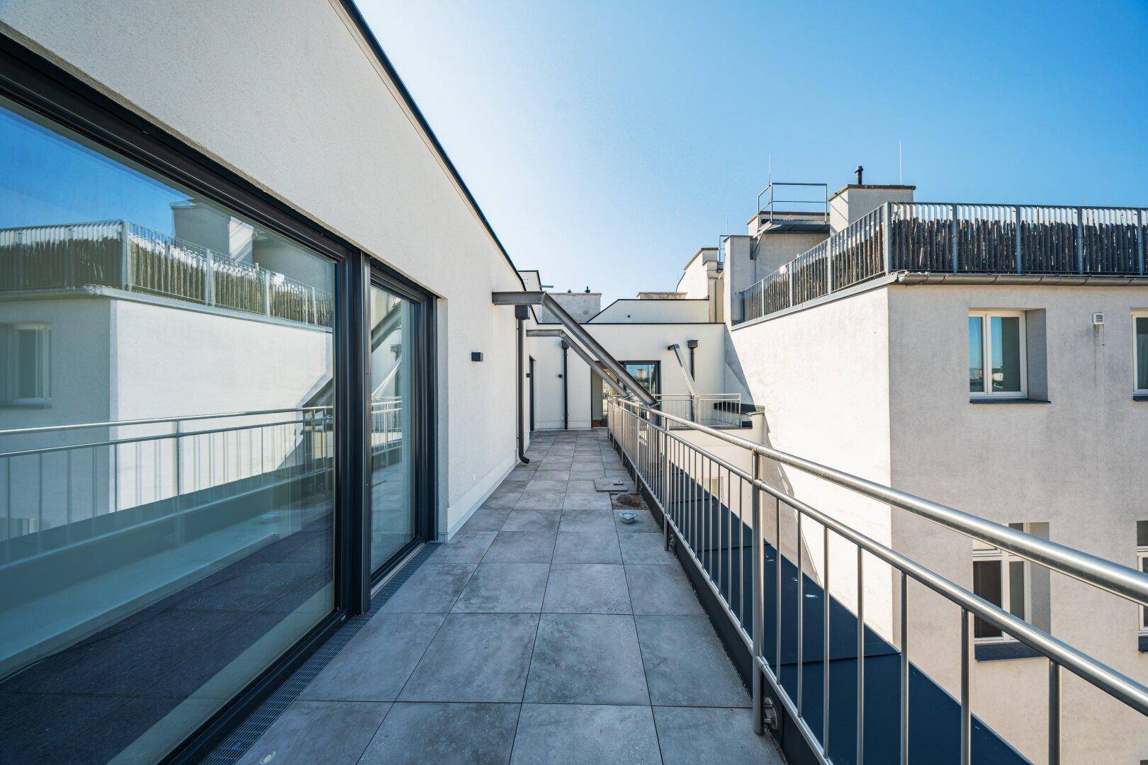 Langer, gefliester Balkon mit großen Glasfronten und moderner Architektur.