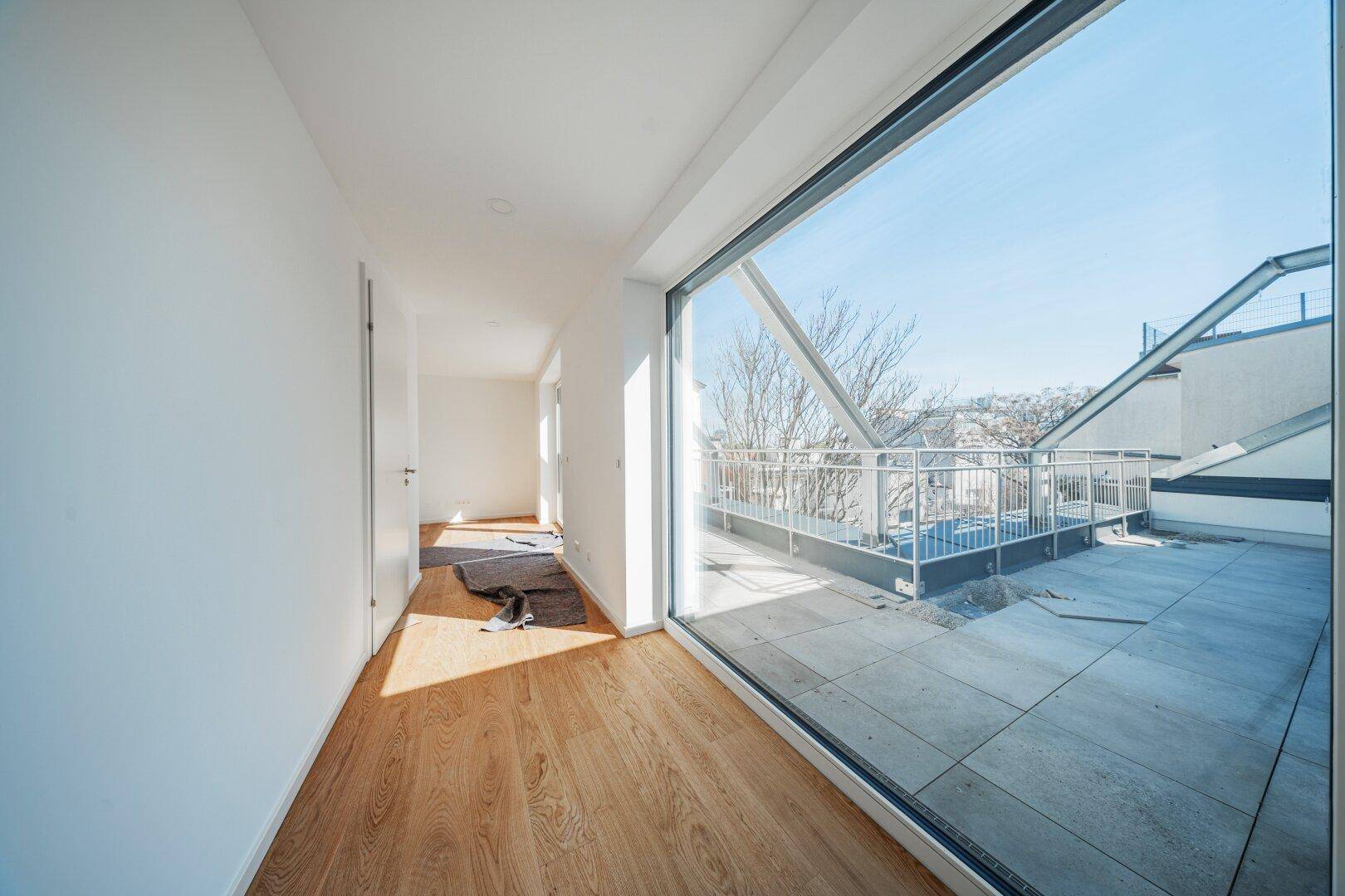 Heller Flur mit Holzboden und raumhoher Verglasung, die den Blick auf die Terrasse freigibt.