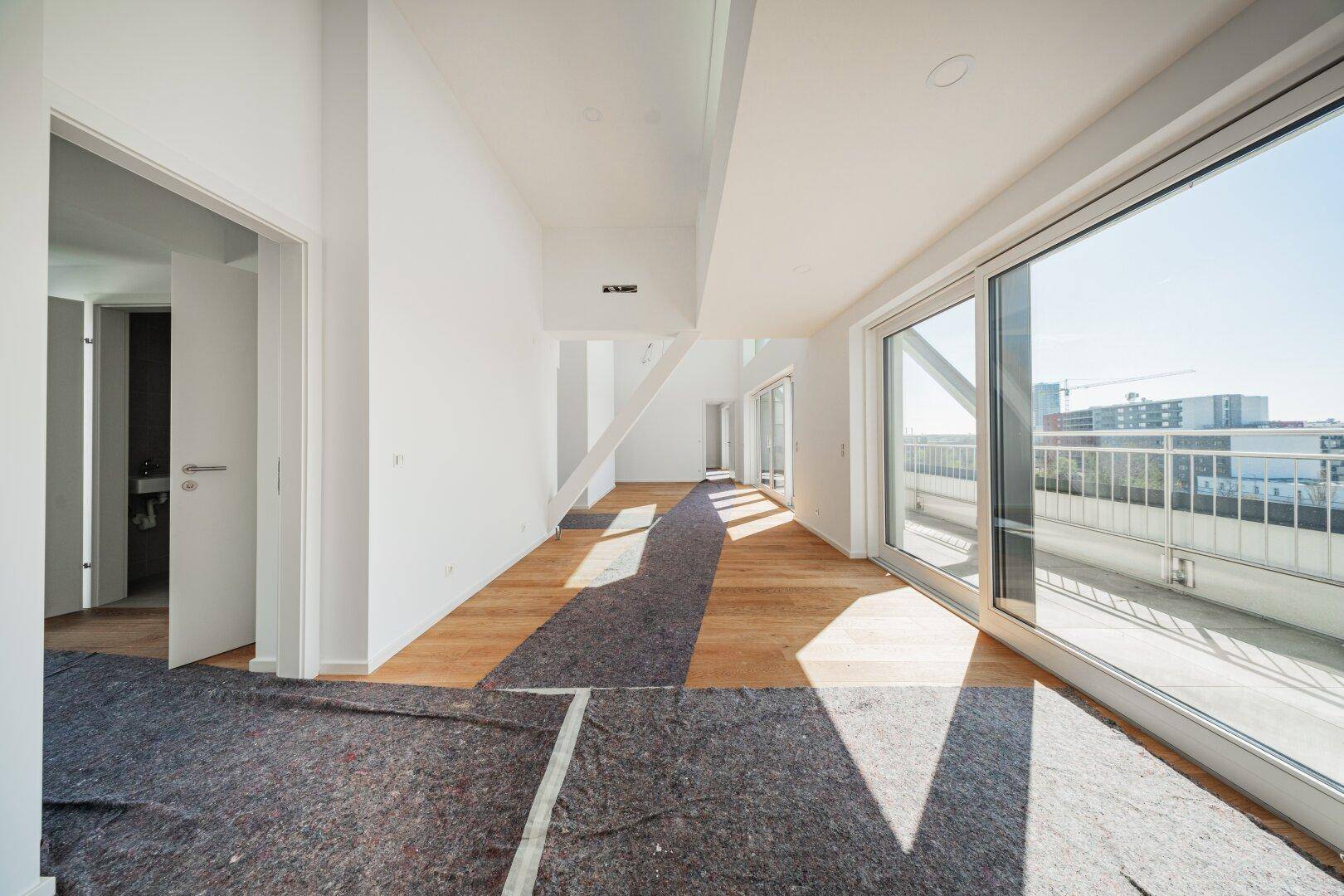 Großzügiger, heller Raum mit Holzboden und breiter Fensterfront, die eine weite Aussicht bietet.