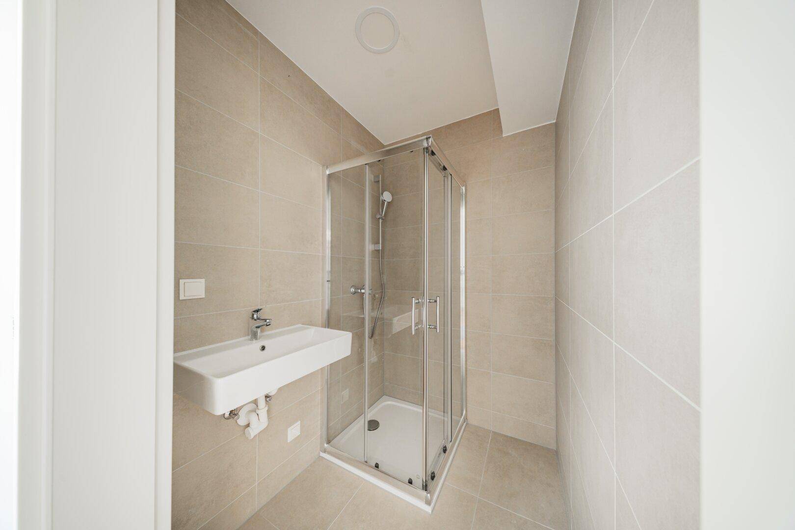 Modernes Badezimmer mit beigefarbenen Fliesen, Duschkabine und Waschtisch.