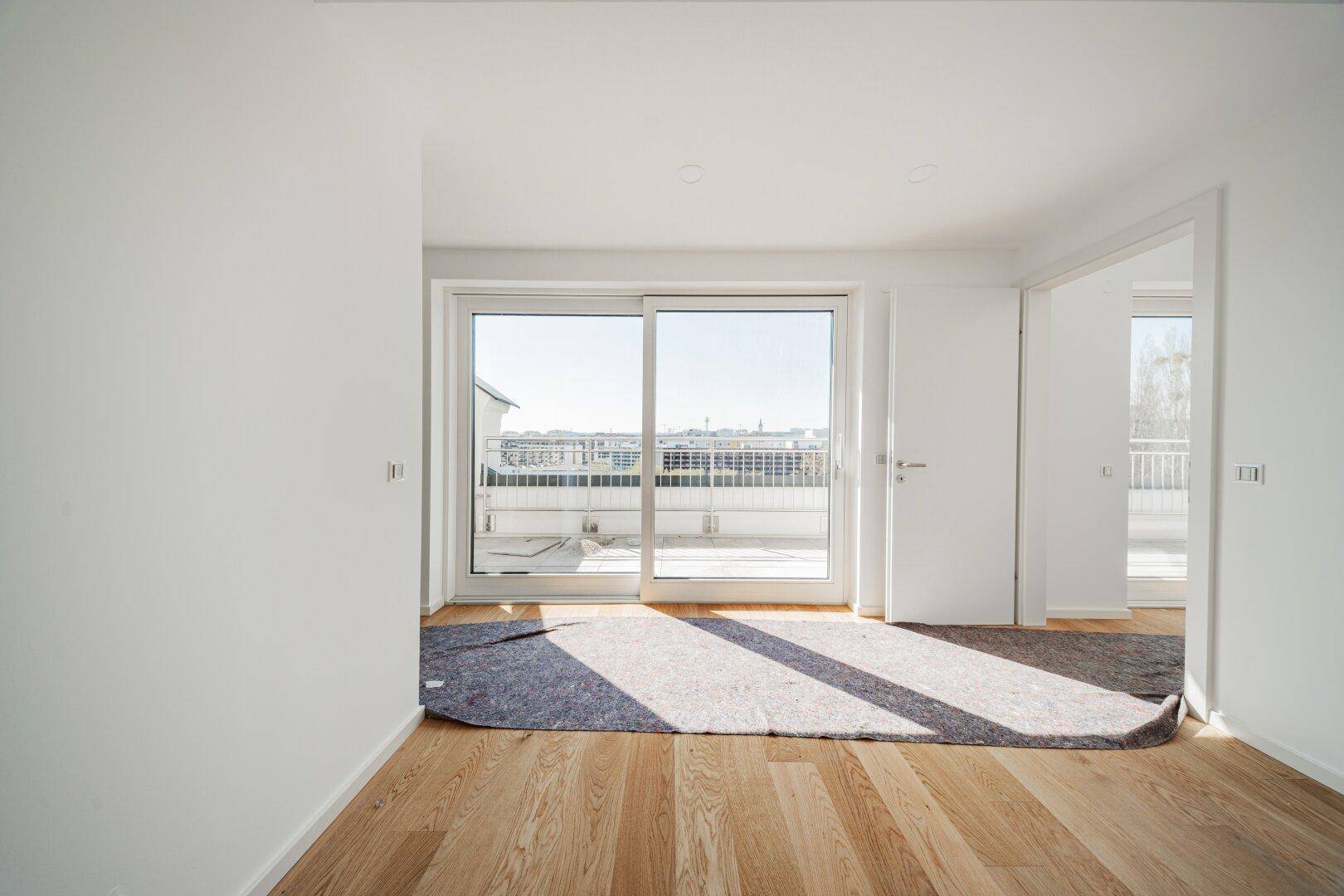 Helles, leeres Zimmer mit Holzboden und Schiebetür zum Balkon, ideal als Schlaf- oder Gästezimmer.