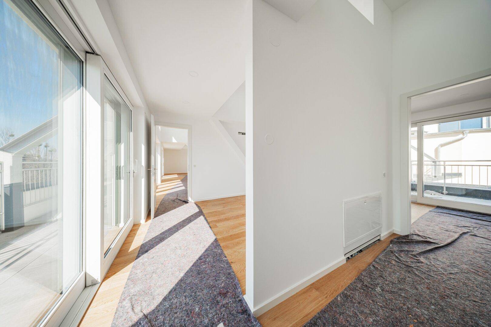 Langer, heller Flur mit Holzboden und großen Fensterfronten, die den Raum mit Licht füllen.