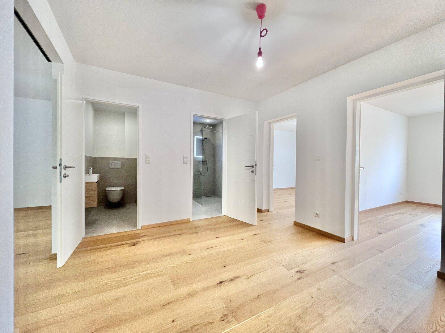 Heller Flur mit Holzboden, der zu einem Gäste-WC und einem modernen Duschbad führt.