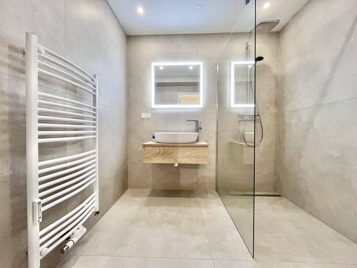 Modernes Badezimmer mit ebenerdiger Dusche, beleuchtetem Spiegel und Handtuchheizkörper.
