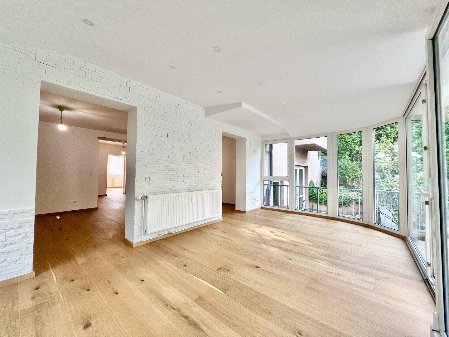 Heller Wohnraum mit Holzboden, dekorativer Ziegelwand und großen Fenstern zum Garten.