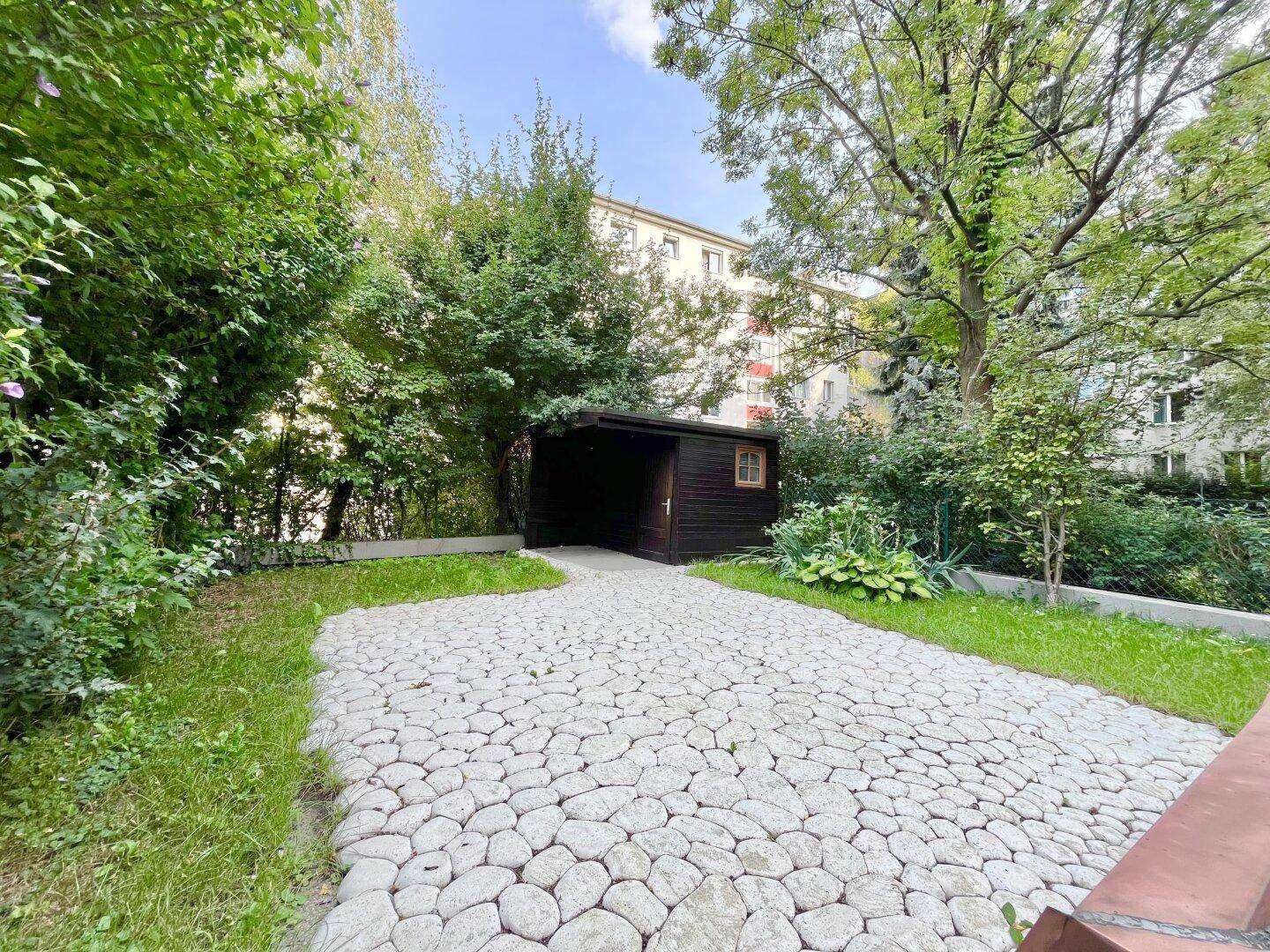 Grüner Garten mit gepflastertem Bereich, Gartenhaus und umgebenden Bäumen.