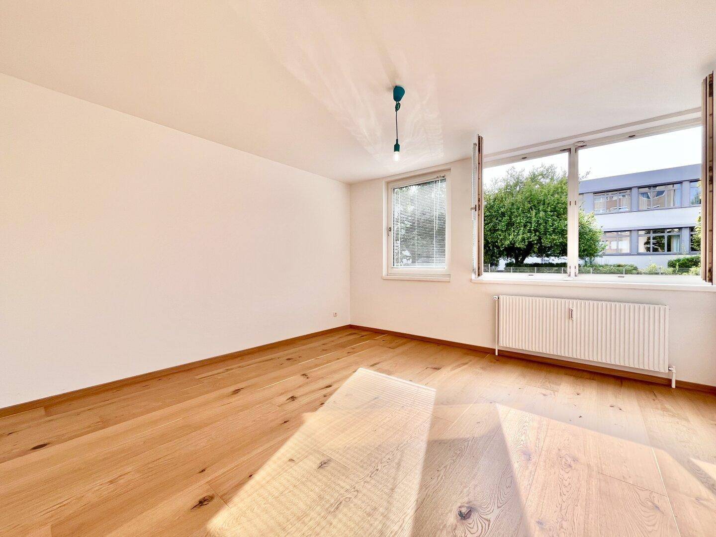 Helles Schlafzimmer mit Holzboden, großen Fenstern und Blick auf die Umgebung.