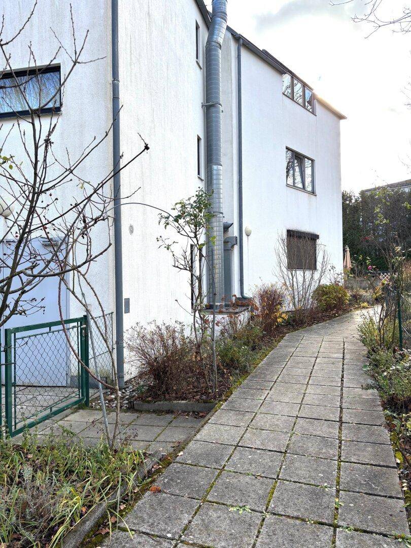 Außenansicht eines weißen Gebäudes mit einem gepflasterten Weg und umliegender Vegetation.