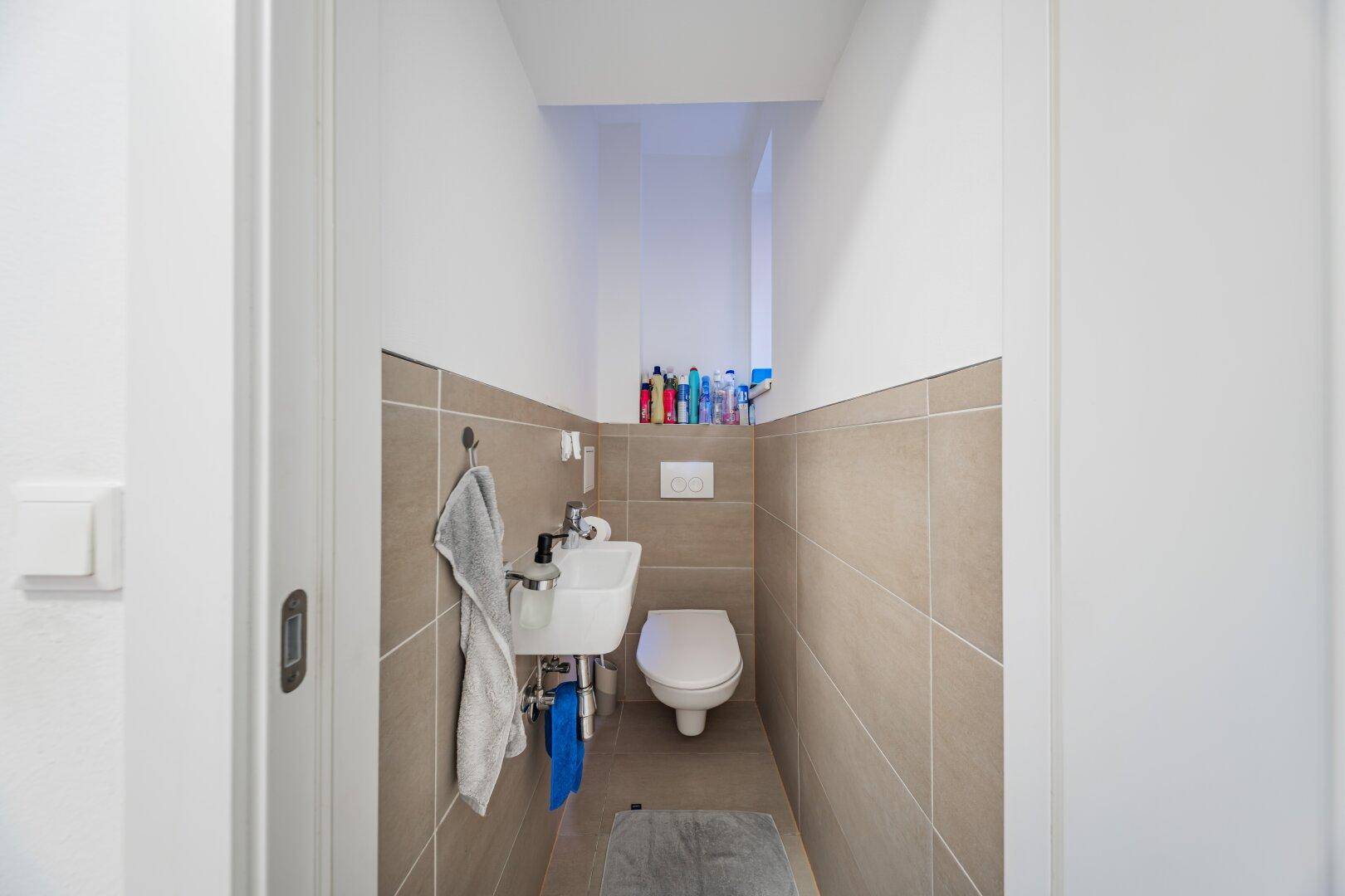 Kompaktes Gäste-WC mit wandhängender Toilette und kleinem Waschbecken, modern gefliest.