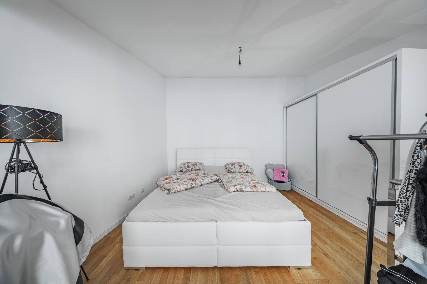 Schlichtes Schlafzimmer mit weißem Bett, Holzboden und großen Schiebetürenschränken.