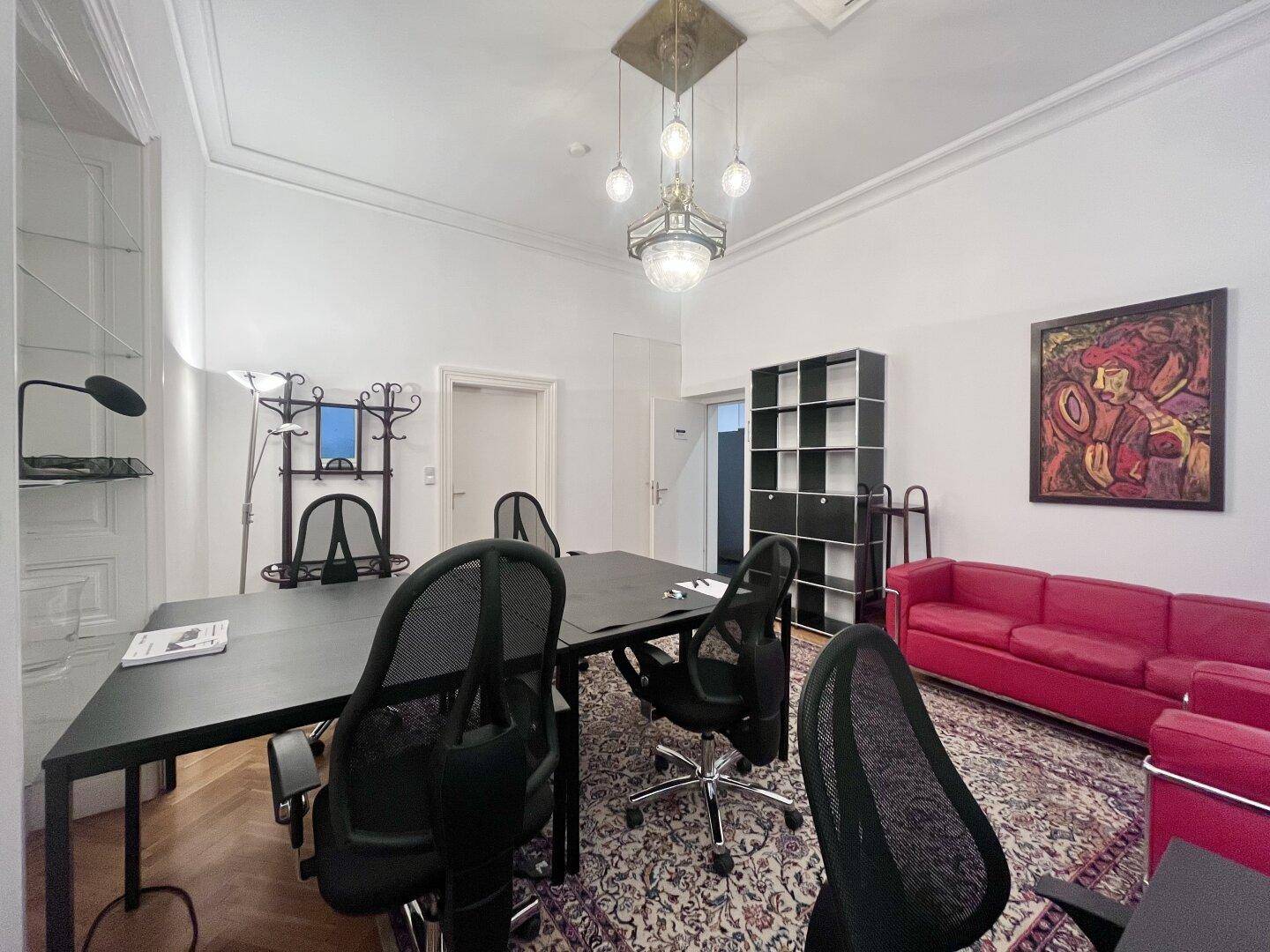 Modern eingerichtetes Büro mit Konferenztisch, rotem Sofa und Kunstwerken an den Wänden.