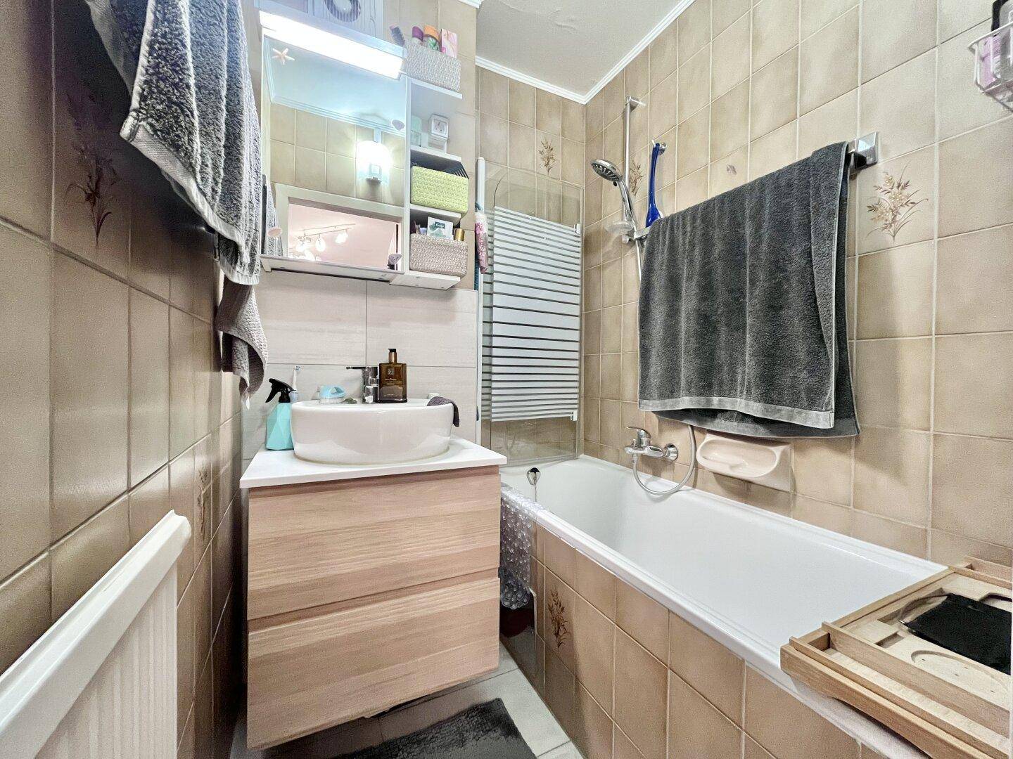 Badezimmer mit Badewanne, Waschbecken und beigefarbenen Fliesen.