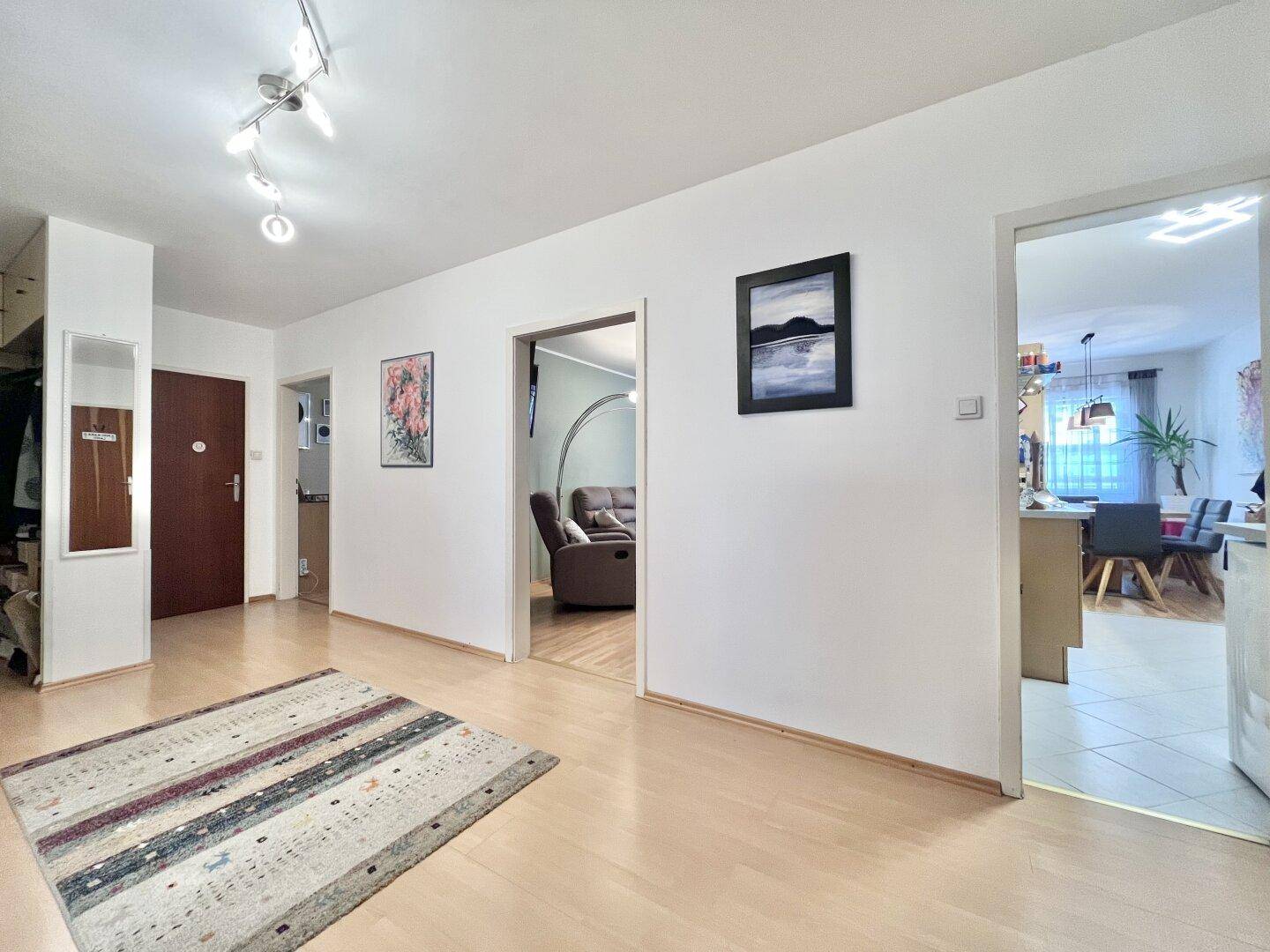 Heller Flur mit Holzboden und Zugang zu verschiedenen Räumen, inklusive Wohnzimmer und Küche.