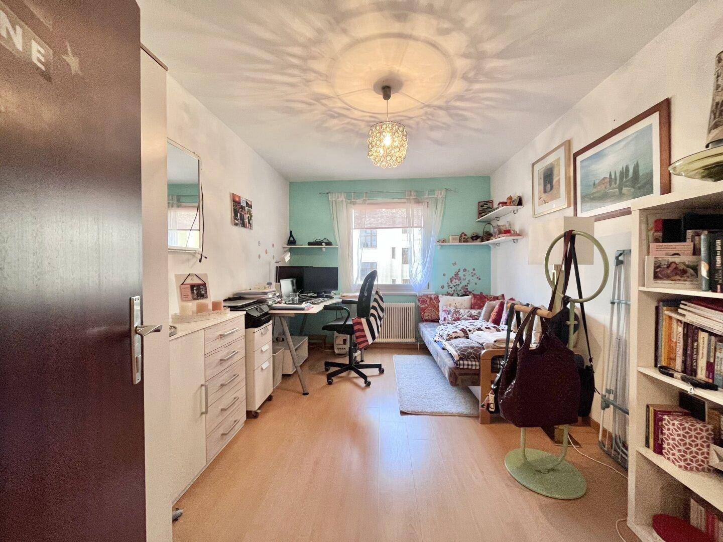 Helles Arbeitszimmer mit Schreibtisch, Bett und farbiger Wandgestaltung.