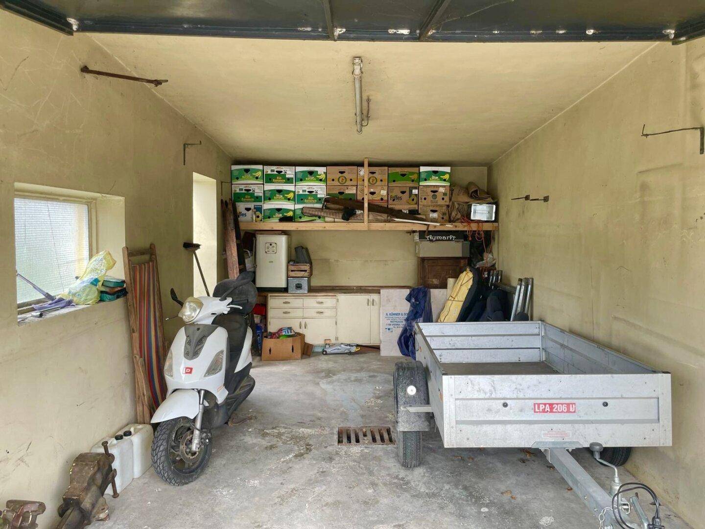 Geräumige Garage oder Abstellraum mit Roller, Anhänger und Lagerregalen.