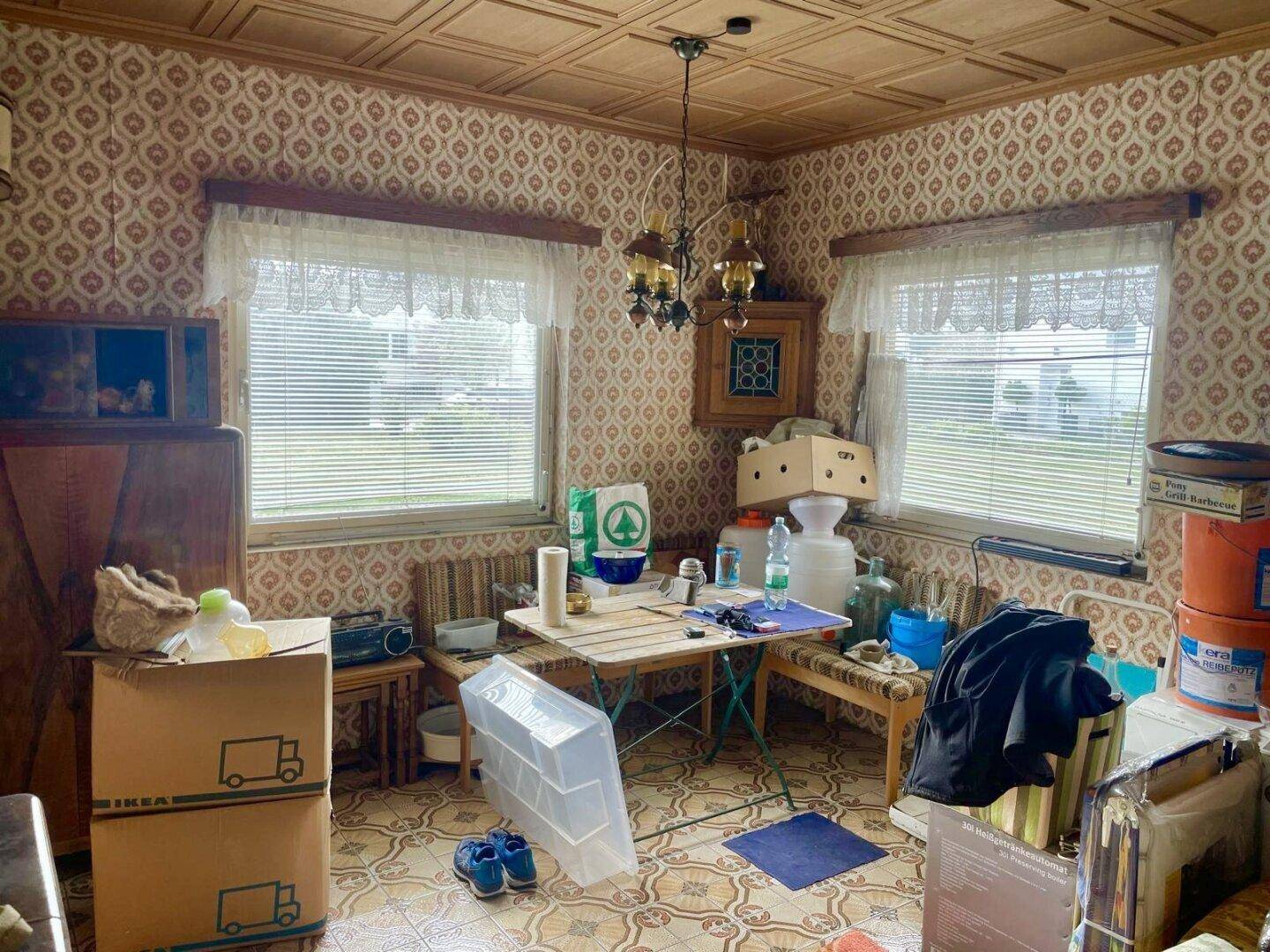 Wohnraum mit gemusterter Tapete, Holzdecke, kleinem Tisch und verschiedenen Gegenständen.