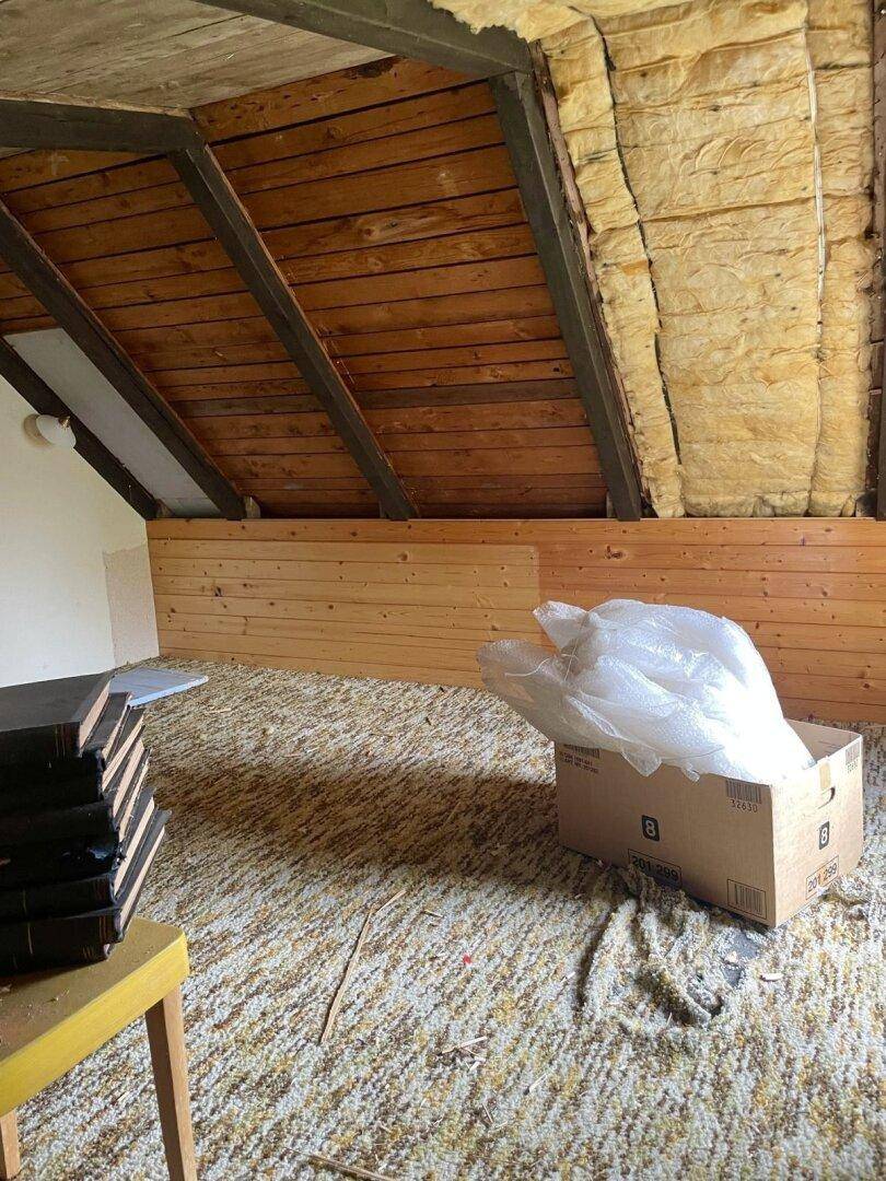 Unausgebauter Dachboden mit sichtbaren Holzbalken, Isolierung und schräger Decke.