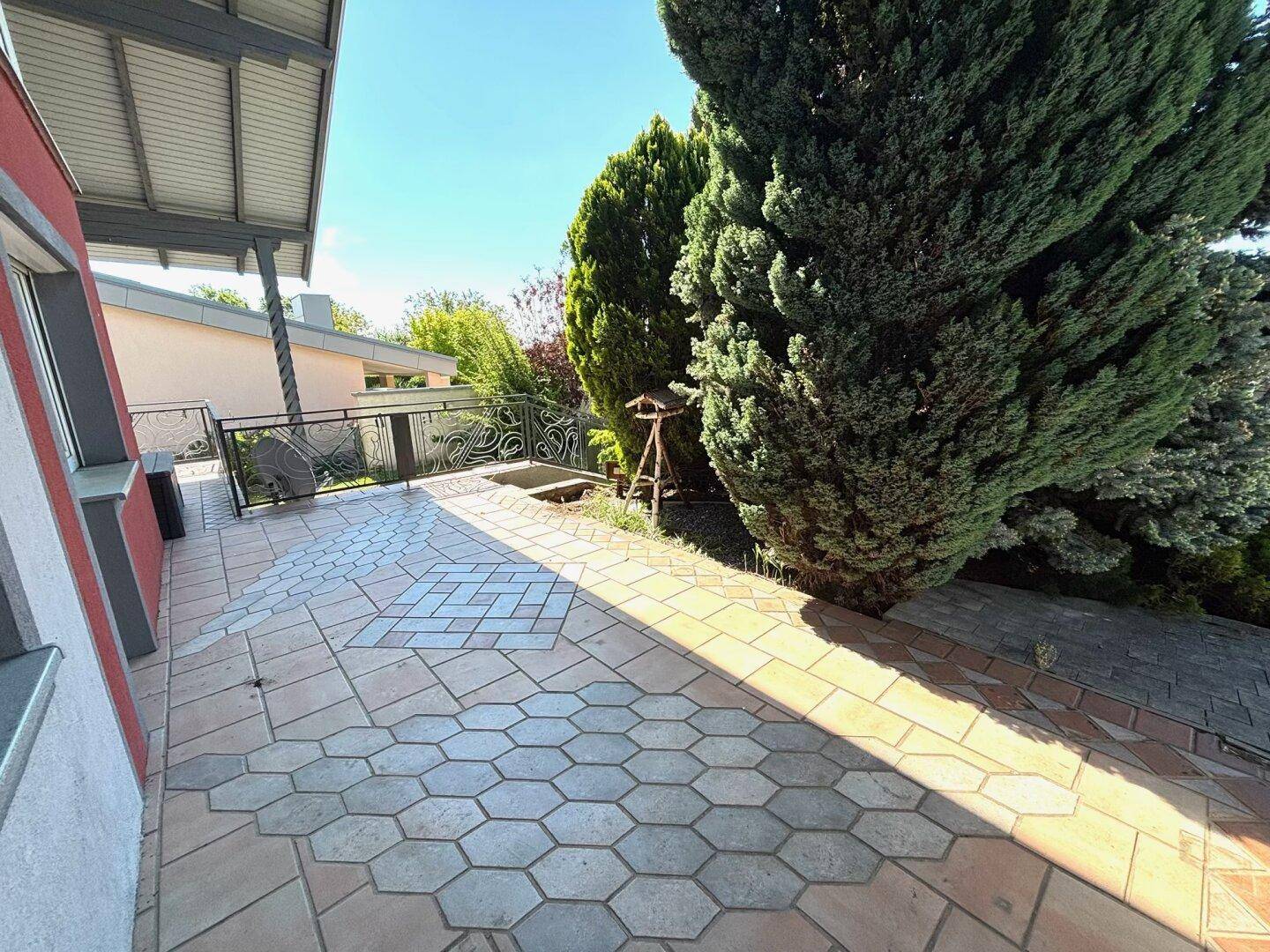 Geräumige, geflieste Terrasse mit dekorativem Muster und viel Grün im Hintergrund.