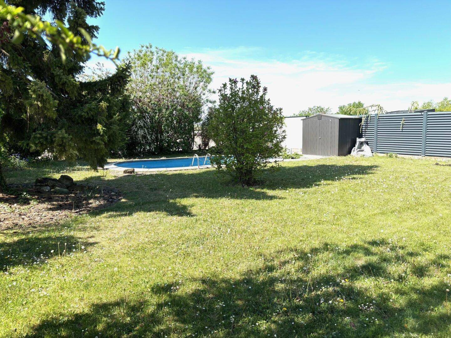 Großer grüner Garten mit Rasenfläche, Bäumen und einem sichtbaren Swimmingpool.