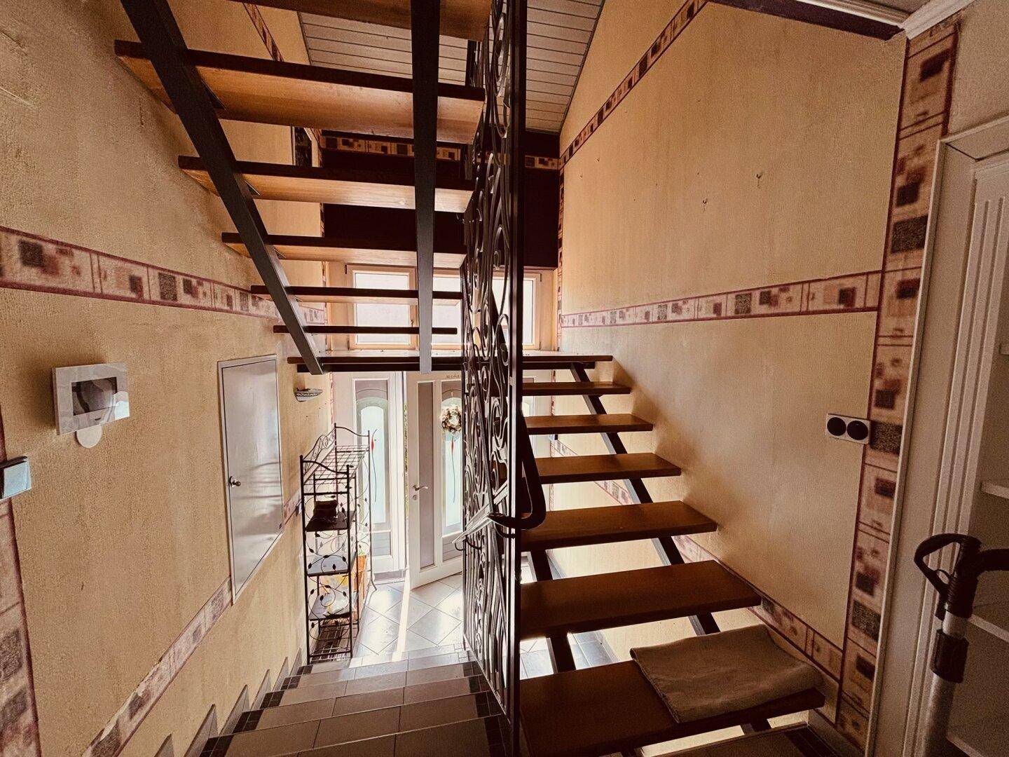 Geräumiger Flur mit Holztreppe und dekorativem Geländer, der zu den oberen Etagen führt.