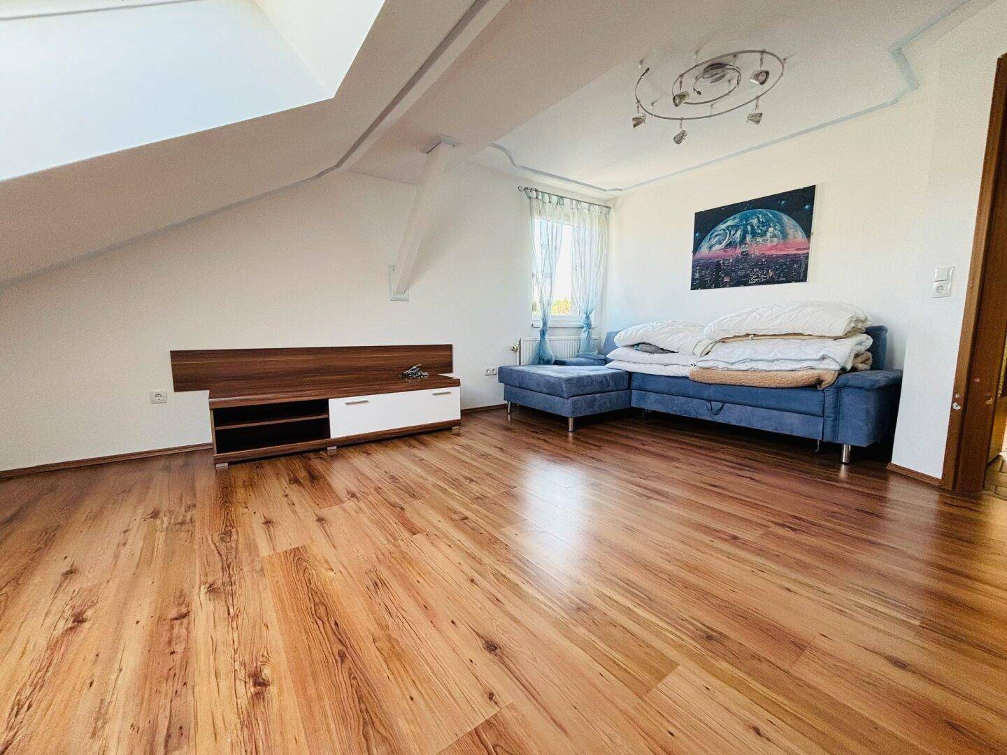 Helles Wohnzimmer im Dachgeschoss mit Laminatboden, Schrägen und gemütlicher Sitzecke.