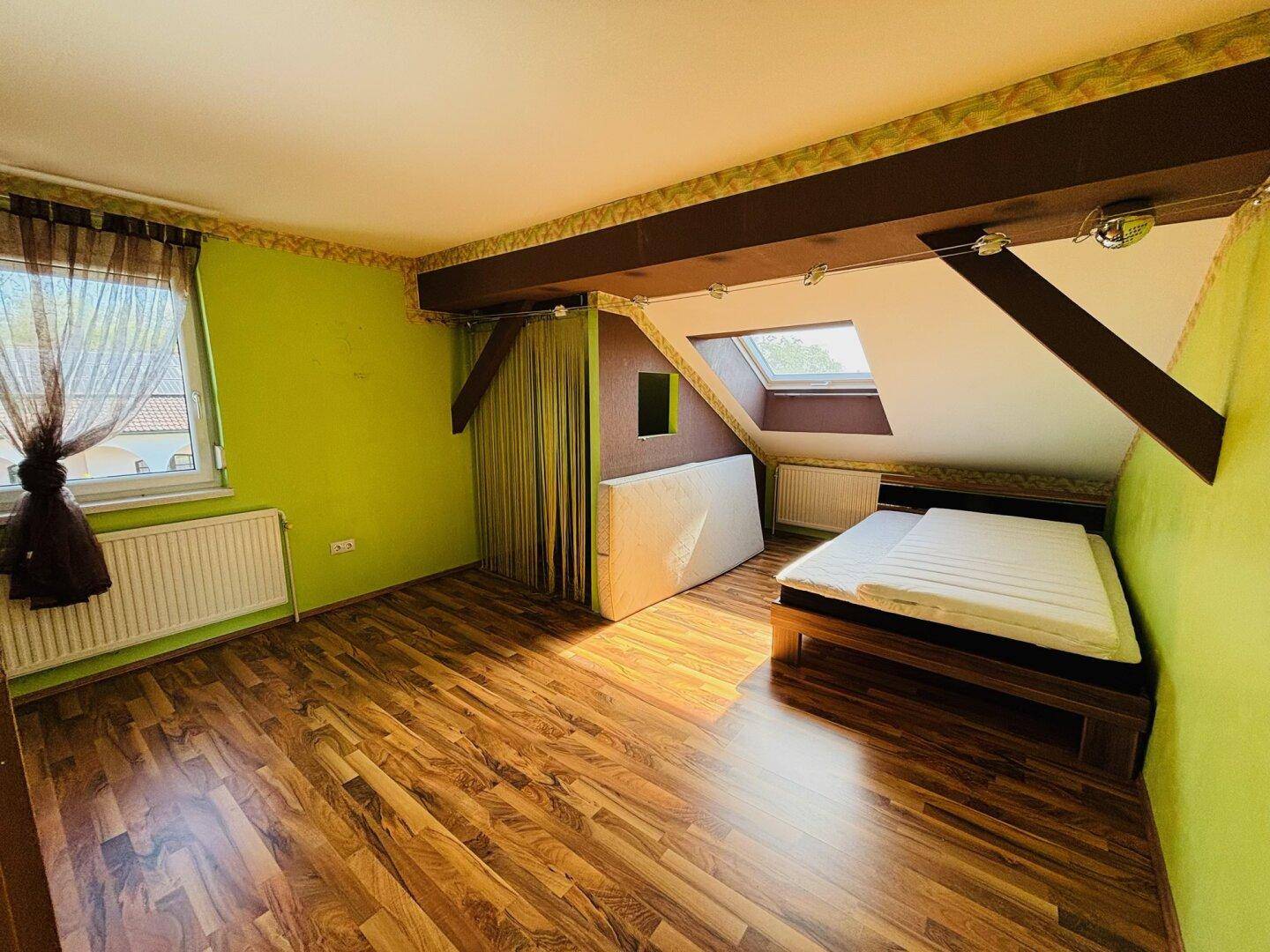 Schlafzimmer im Dachgeschoss mit Holzbalken, Laminatboden und Dachfenster.