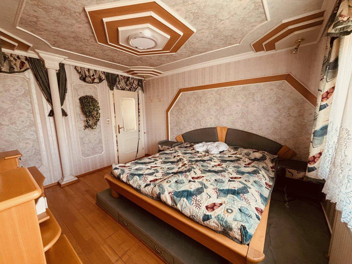 Schlafzimmer mit Holzboden, dekorativer Decke und einem großen Doppelbett.