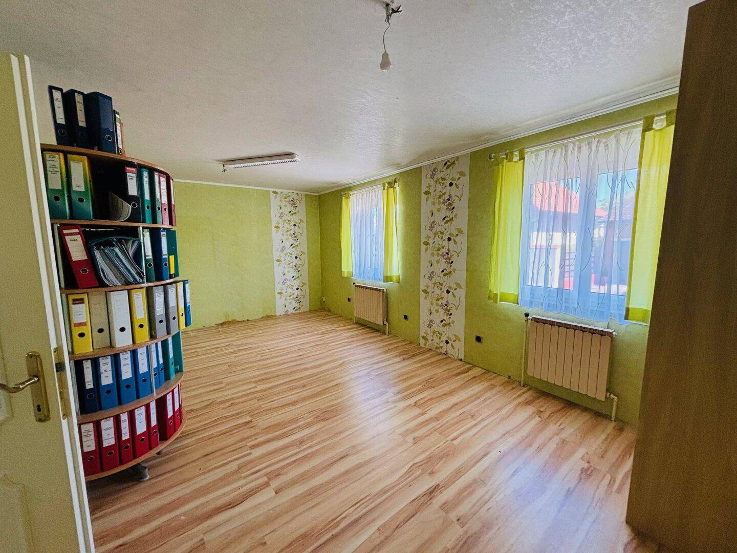 Helles Arbeitszimmer mit Laminatboden, grünen Wänden und großem Bücherregal.