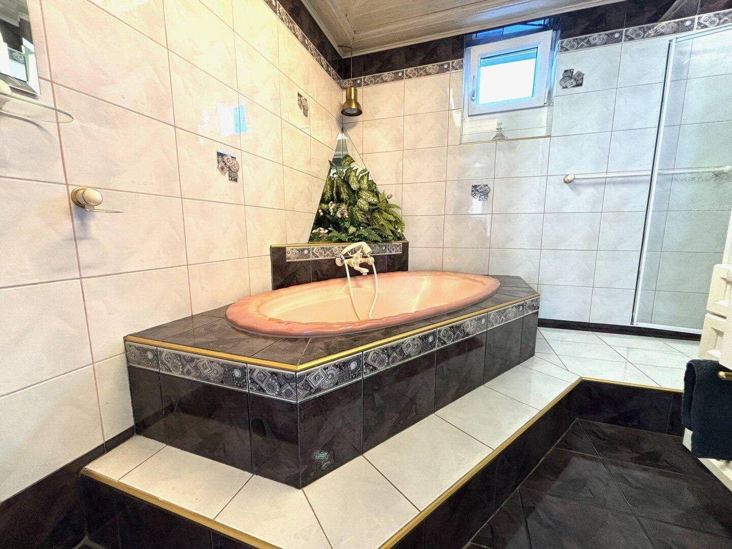 Badezimmer mit erhöhter Badewanne, Fliesenboden und Duschkabine im Hintergrund.