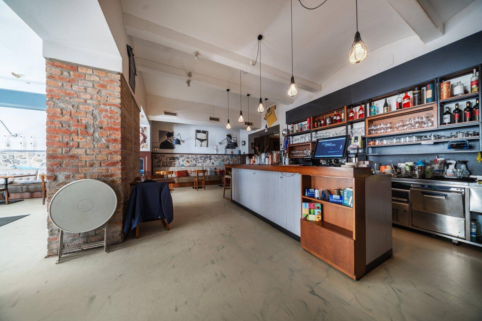 Barbereich mit Backsteinwand, Theke und Regalen voller Flaschen, angrenzend an den Gastraum.