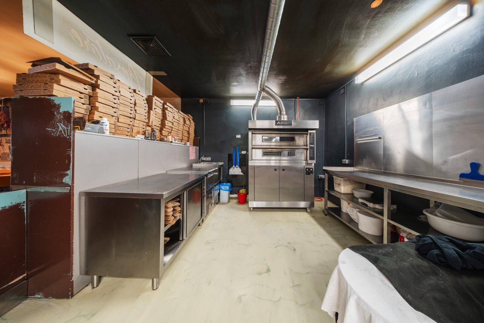 Professionelle Pizzaküche mit großem Ofen, Edelstahlarbeitsflächen und dunkler Decke.