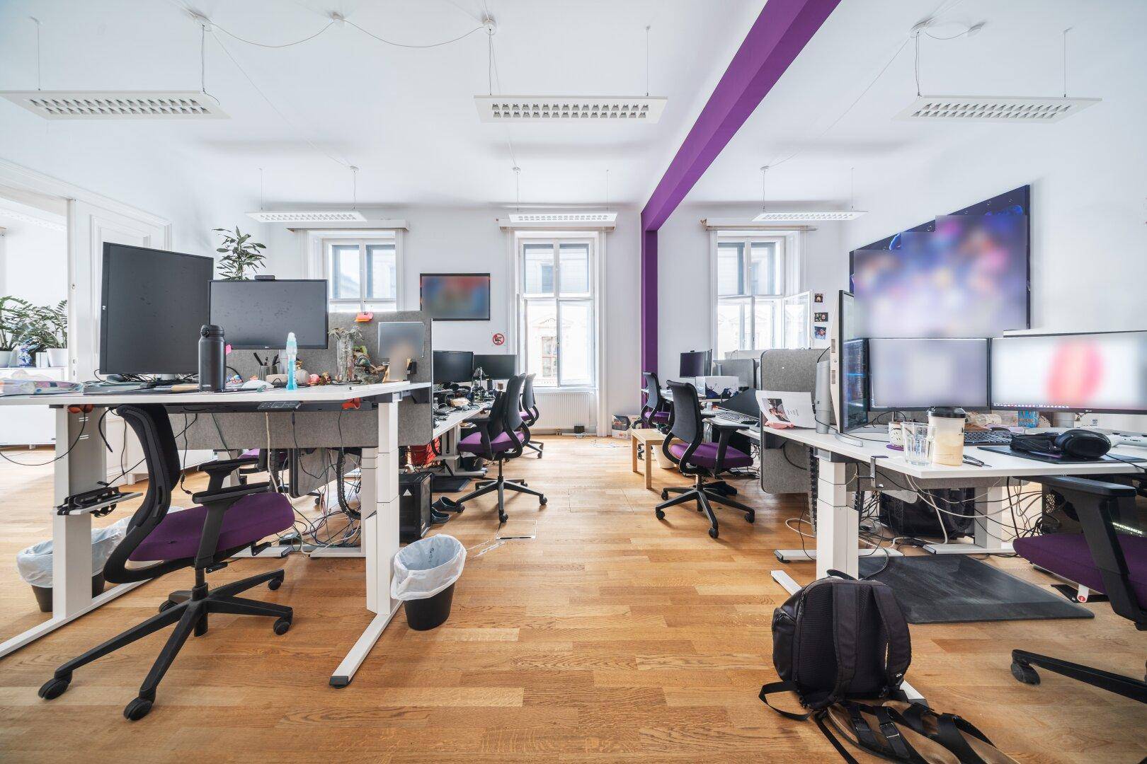 Offenes Büro mit mehreren Arbeitsplätzen, Holzboden und einer lila Akzentwand, die den Raum belebt.