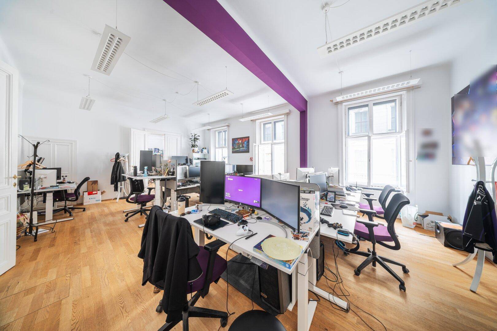Geräumiges Büro mit Holzboden, vielen Arbeitsplätzen und einer auffälligen lila Akzentwand.