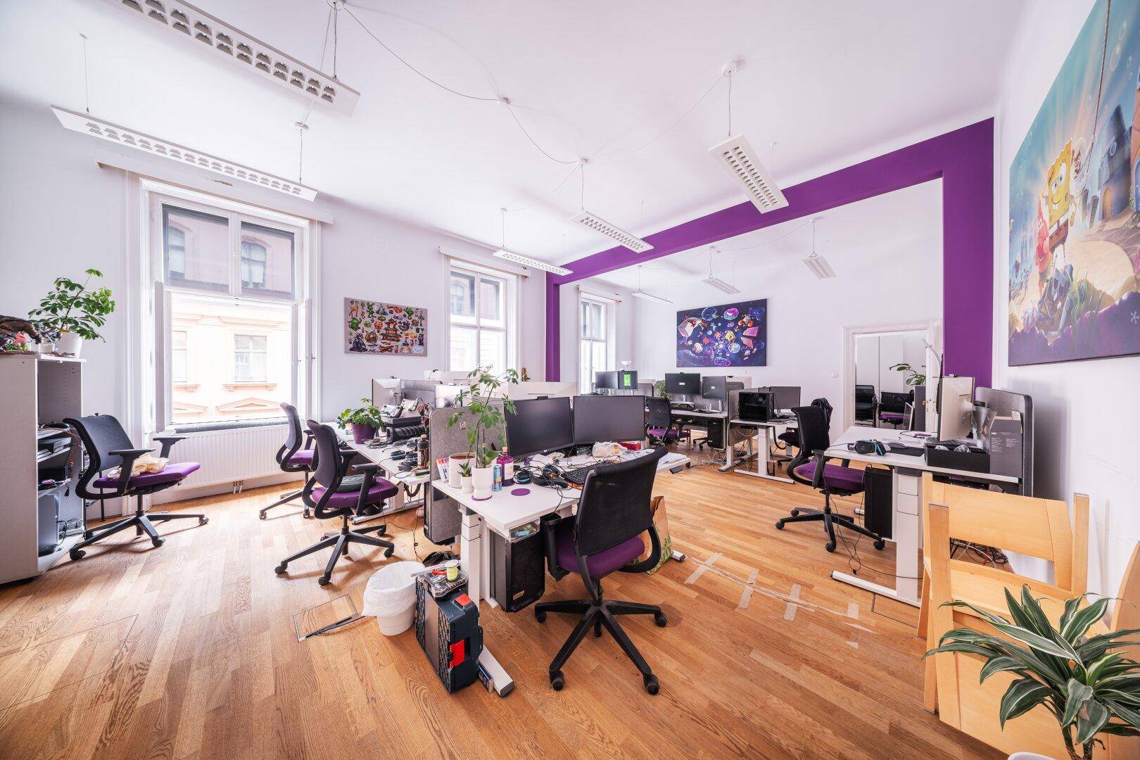 Großes, offenes Büro mit Holzboden, lila Akzentwand und mehreren Arbeitsplätzen mit Monitoren.