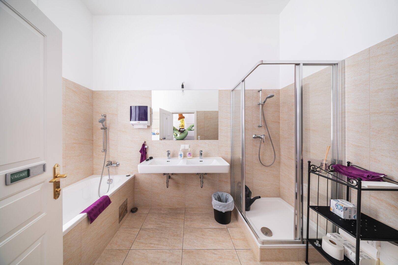 Helles Badezimmer mit Badewanne, Duschkabine, Doppelwaschbecken und beigefarbenen Fliesen.