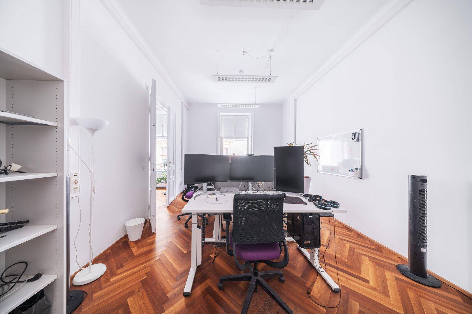 Einzelbüro mit Fischgrätparkett, einem großen Schreibtisch und einem Fenster mit Blick nach draußen.