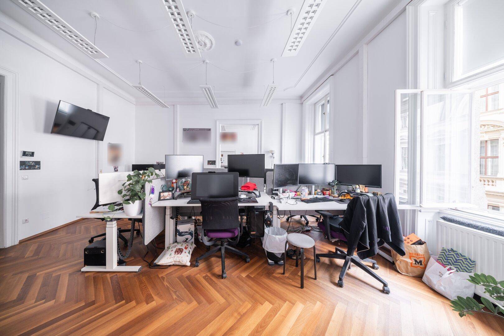 Großes, offenes Büro mit mehreren Arbeitsplätzen, Fischgrätparkett und hohen Fenstern.