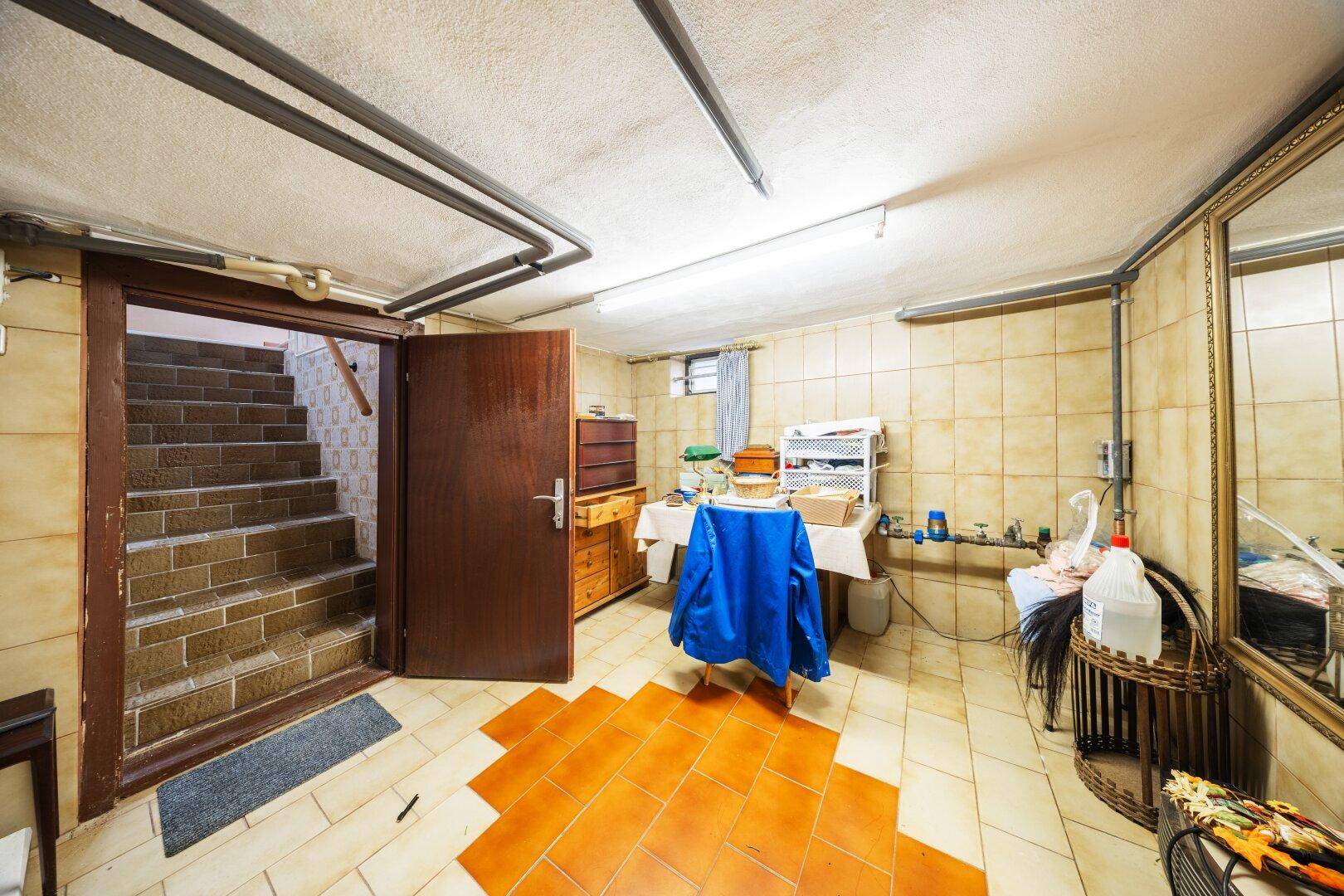 Kellerraum mit Fliesenboden, Lagerregalen und Zugang zur Treppe.