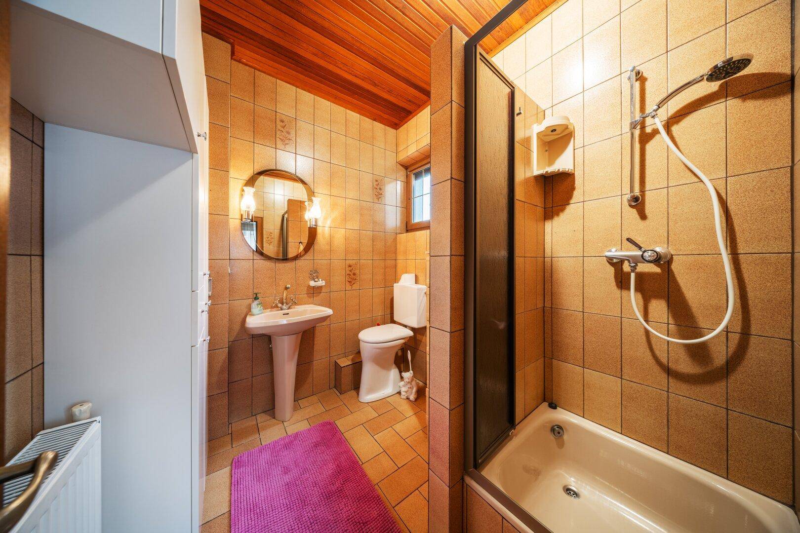 Badezimmer mit braunen Fliesen, Duschwanne und Einzelwaschbecken.