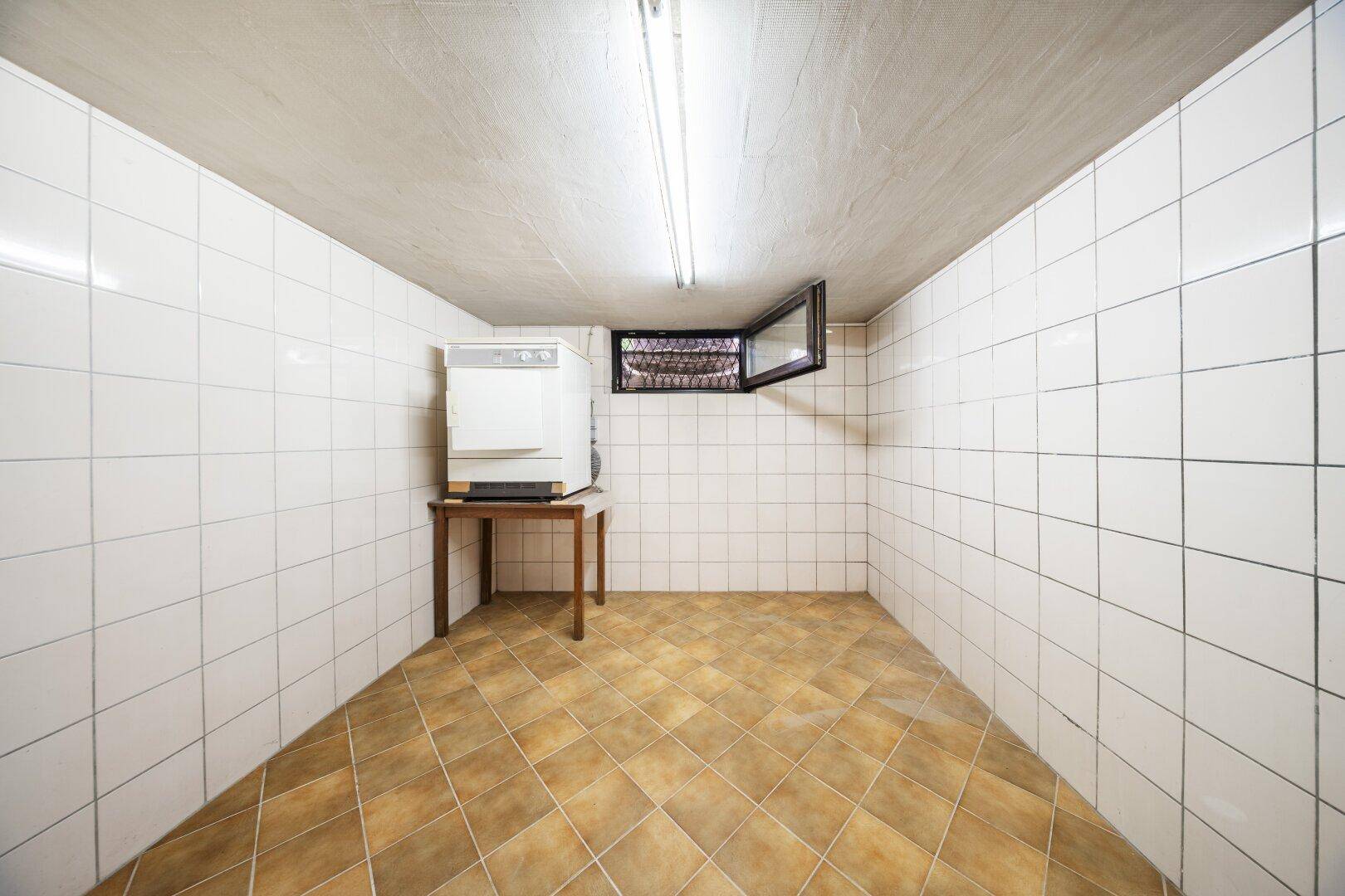 Geräumiger, gefliester Kellerraum mit kleinem Fenster und Waschmaschine.