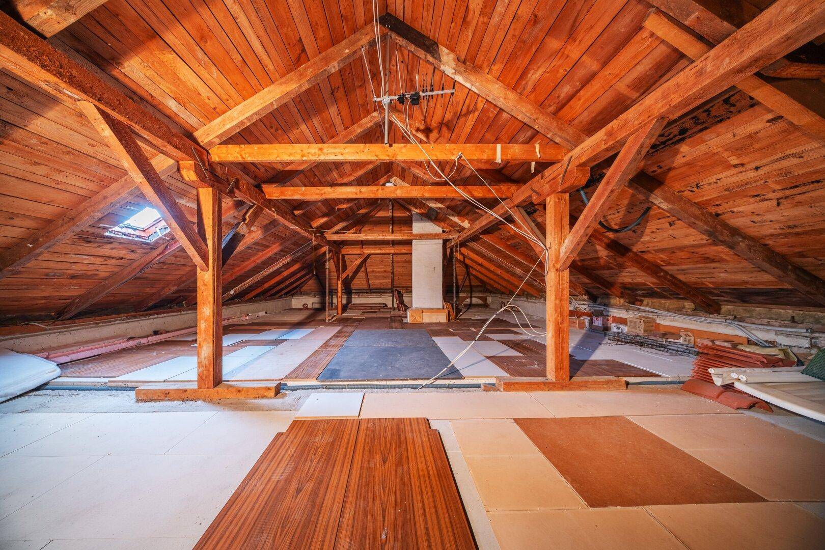Geräumiger Dachboden mit sichtbaren Holzbalken und Dachfenster, bereit für Ausbau.