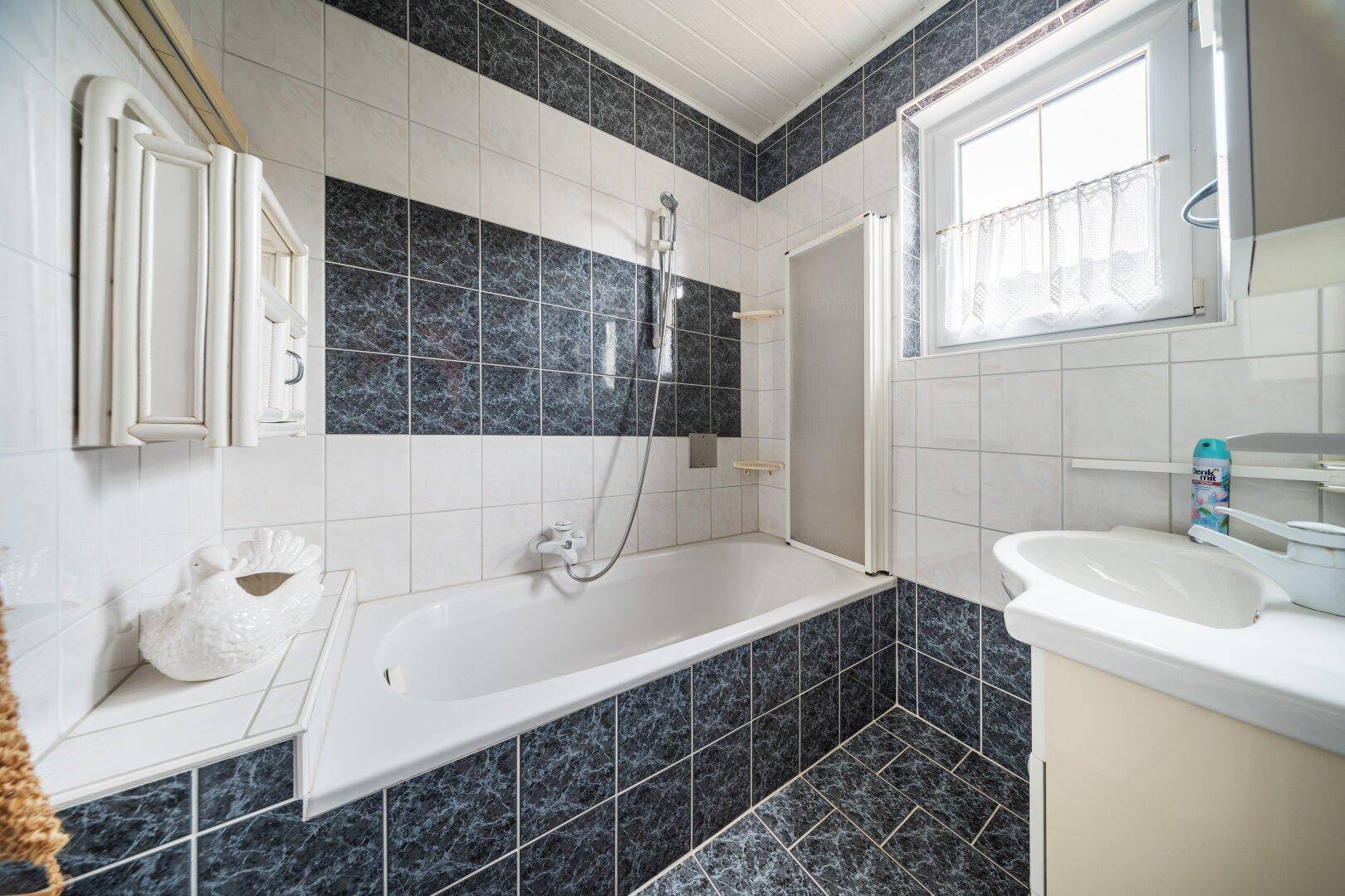 Badezimmer mit schwarz-weißen Fliesen, Badewanne und Fenster.