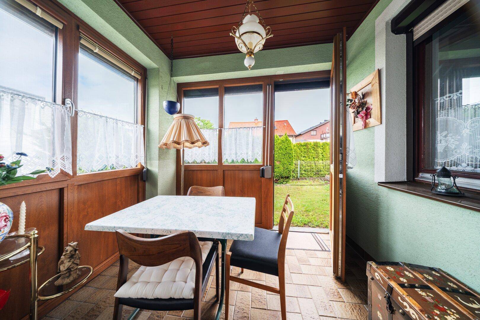 Heller Wintergarten mit Esstisch, Stühlen und Blick in den Garten.