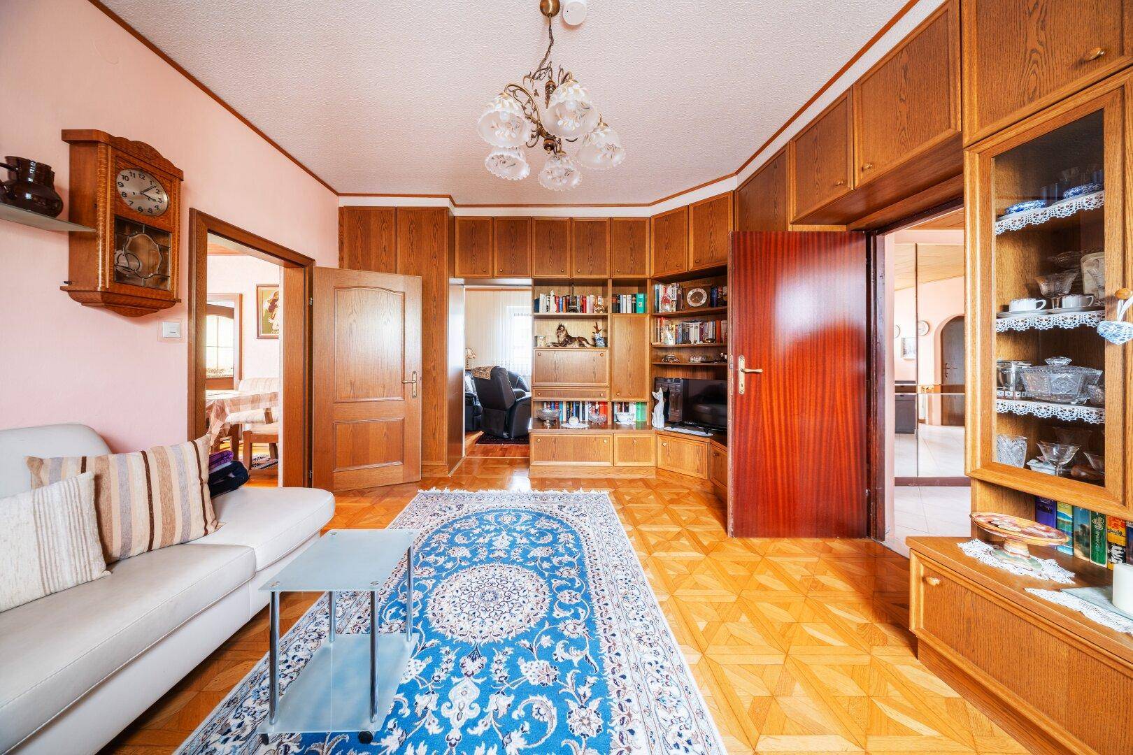 Wohnzimmer mit beiger Eckcouch, Holzeinbauten und traditionellem Teppich.