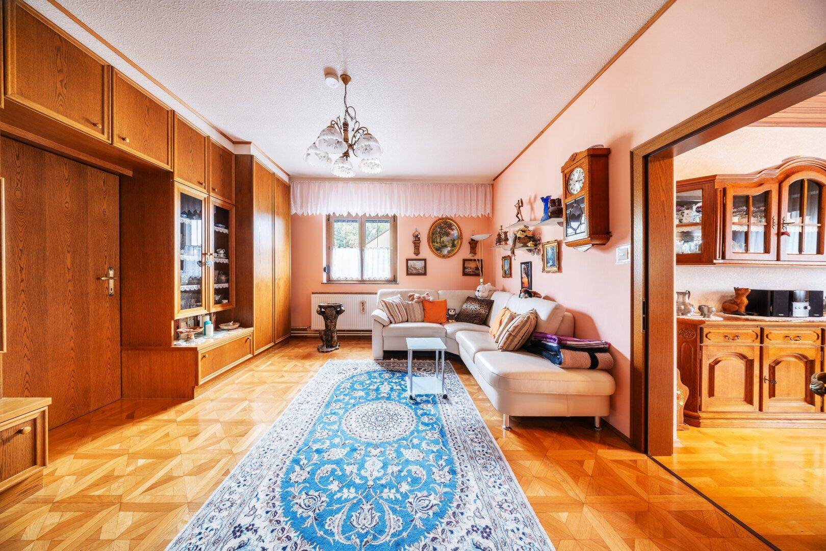 Geräumiges Wohnzimmer mit beiger Couch, Holzeinbauten und traditionellem Teppich.