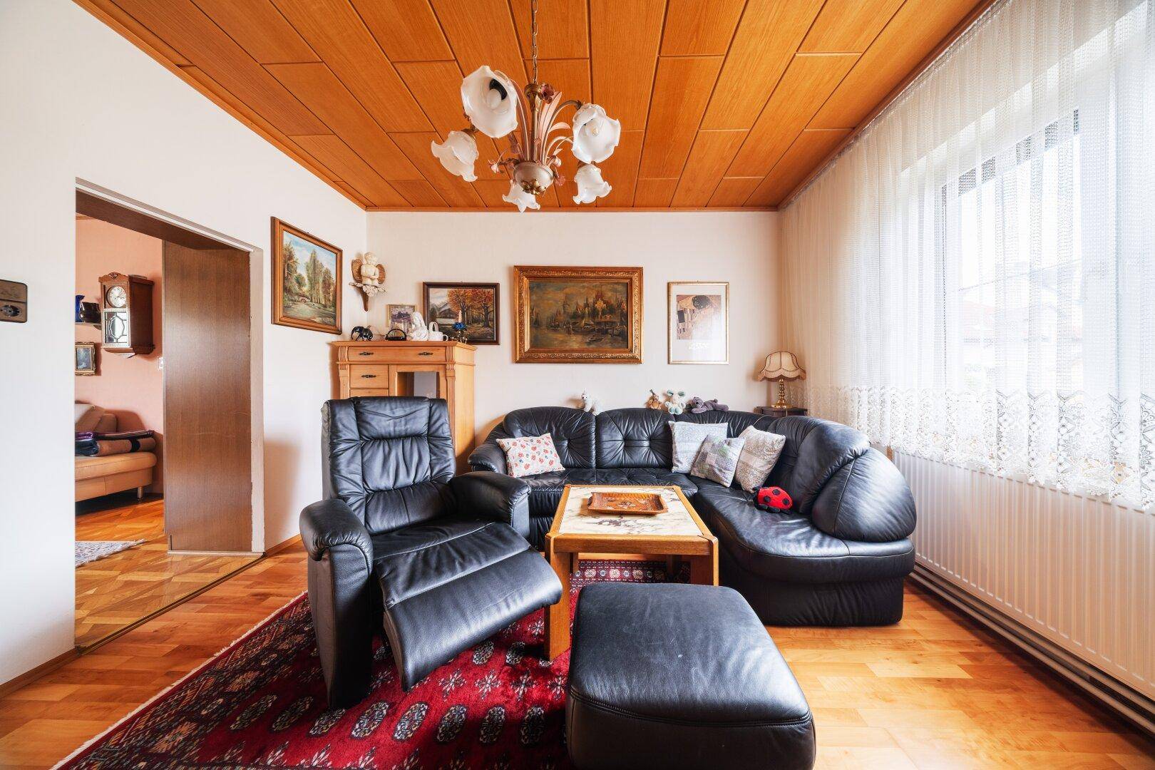 Wohnzimmer mit dunkler Ledercouch, Holzdecke und traditionellen Möbeln.
