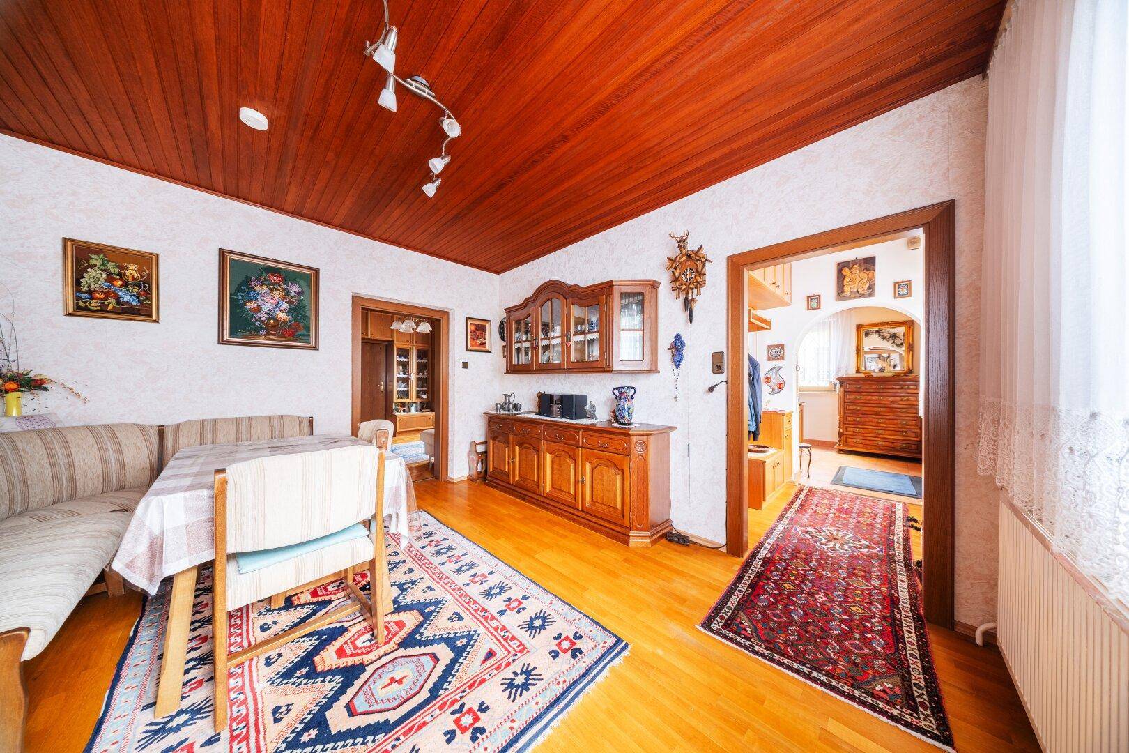 Esszimmer mit Holztäfelung an der Decke, Esstisch und Sitzbank in traditionellem Stil.